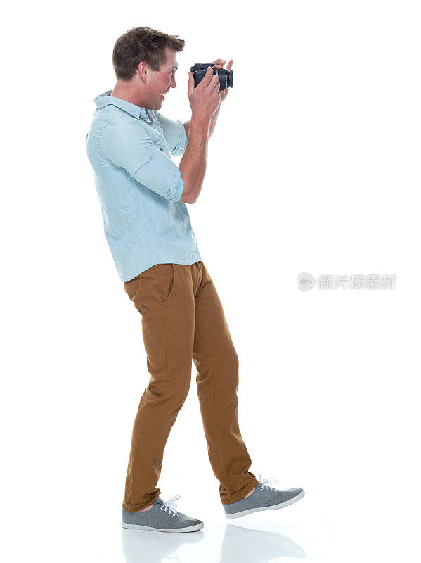 一人/全长/侧视图20-29岁英俊的人/短发白人男性/年轻男子摄影师/摄影在白色背景穿着纽扣衬衫/裤子谁正在拍照